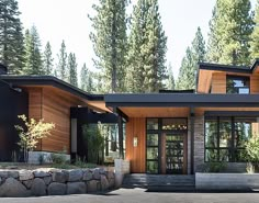 a modern house in the woods with large windows and stone walls on both sides, surrounded by pine trees