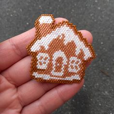 a hand holding a brown and white beaded ornament with a house on it