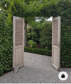 an open wooden door in the middle of a graveled area surrounded by greenery