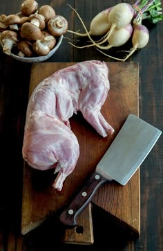 raw chicken sitting on a cutting board next to garlic, mushrooms and a large knife