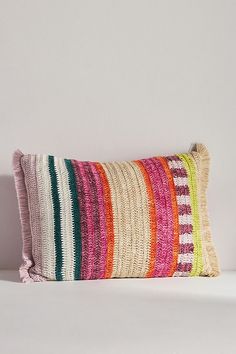 a multicolored striped pillow sitting on top of a white bed next to a wall