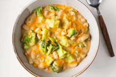 a white bowl filled with broccoli and cheese next to a spoon on top of a table