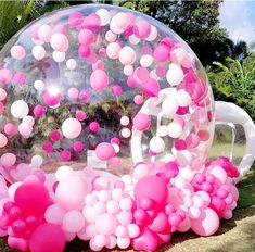 a large bubble filled with pink and white balloons on top of a grass covered field