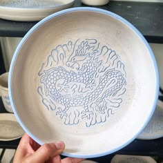 a person holding up a white and blue bowl with a dragon design on the side