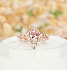 a pink diamond ring sitting on top of a white cloth covered box with flowers in the background