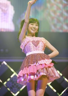 a woman in a pink and white dress on stage with her hand up to the sky