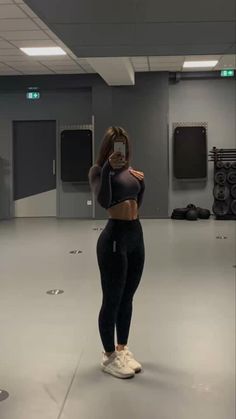 a woman taking a selfie with her cell phone in an empty gym room filled with exercise equipment