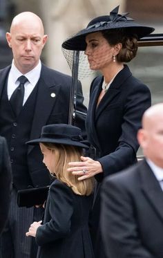 two women and a man in black suits are standing together with hats on their heads