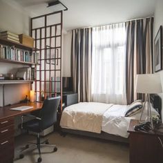 a bedroom with a bed, desk and bookcase in front of a large window