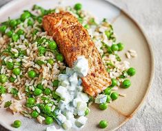 a white plate topped with rice, peas and salmon on top of a bed of sauce