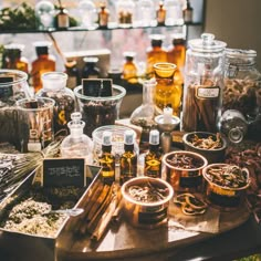 an assortment of spices and herbs on a table in front of shelves full of bottles