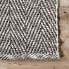 a gray and white knitted rug on top of a wooden floor next to a pair of scissors