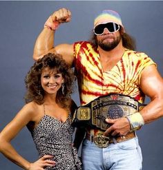 a woman standing next to a man with a wrestling belt on his chest and wearing sunglasses