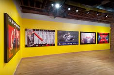 an empty room with paintings on the wall and wooden floors in front of yellow walls