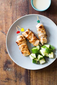 chicken and cucumber skewers on a white plate next to a cup of milk