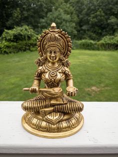 a golden statue sitting on top of a white table next to a lush green field