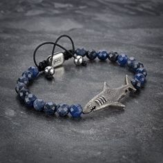 Make a statement with this 925 Silver Shark Bracelet made with 6 mm Sodalite beads. Crafted with precision, our signature 925 silver shark bead introduces a touch of the ocean's mystique into your accessory collection. The bracelet is adjustable with a sliding knot made of macrame string for a comfortable and secure fit. Expertly handcrafted with attention to detail and high-quality materials, this unique piece comes in a black gift box. DESIGNER'S REMARKS Discover the enchanting beauty of gemstones, crafted over millions of years by Earth's intricate geological processes. Adorning your wrist with Juniper & Eloise Jewelry bracelets, you cradle a fragment of the cosmos, resonating with the celestial origins of the elements nestled within these mesmerizing stones, born from distant stars. ST Silver Lapis Lazuli Bracelet, Hand-strung, Silver Lapis Lazuli Hand-strung Bracelets, Silver Hand-strung Lapis Lazuli Bracelet, Silver Lapis Lazuli Hand-strung Beaded Bracelets, Beaded Shark, Shark Bracelet, Mens Onyx Bracelet, Gifts For Him Christmas, Silver Shark