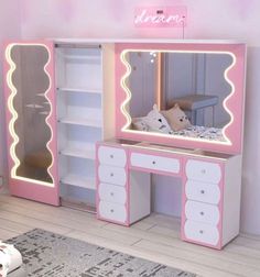 a pink and white dressing table with lights on the top, drawers and mirror in front of it