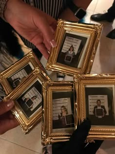 four gold framed pictures are being held by two hands