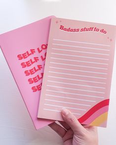 two pink notebooks with writing on them, one being held up by a hand