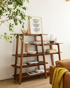 a wooden shelf with books and vases on it in front of a tree branch