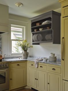 a kitchen with yellow cabinets and white counter tops is pictured in this image, there are dishes on the shelves above the sink