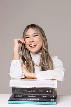 a woman sitting on top of three books with her hand on her chin and smiling