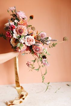 a woman holding a bouquet of flowers on top of a wooden table in front of a pink wall