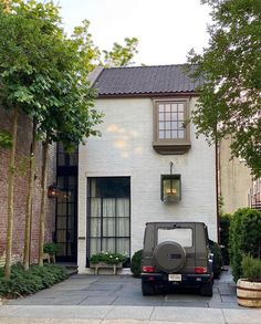 a jeep is parked in front of a white brick house with trees and bushes around it