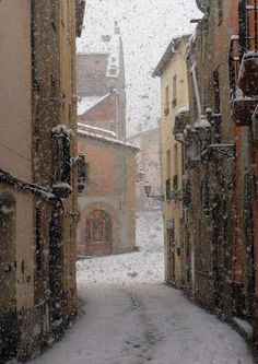 an alley way with snow falling on the ground and buildings in the background, as seen from behind