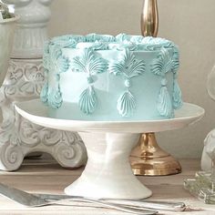 a blue frosted cake sitting on top of a white cake plate next to silverware