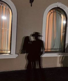 the shadow of a man in a cowboy hat standing next to two windows with curtains