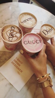 three cups of coffee with the word gucci written on them are being held by two hands