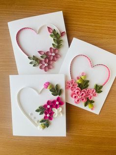 three cards with flowers and hearts made out of paper on a wooden table, one is white and the other is pink