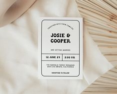 a close up of a wedding card on a bed with white sheets and wood sticks