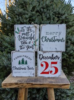 three wooden christmas signs sitting on top of a wooden bench in front of a tree