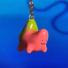 a pink and green toy hanging from a metal chain on a blue background with a black cord