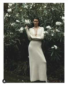 a woman standing in front of a bush with white flowers