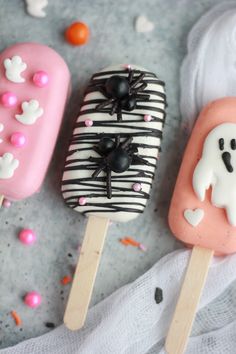 three popsicles decorated with icing and sprinkles on top of a table