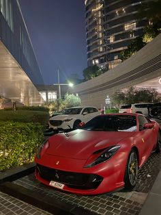 a red sports car parked in front of a building at night with other cars behind it