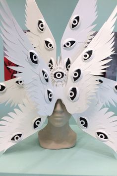 a white mask with black and white feathers on it's face, surrounded by eyeballs