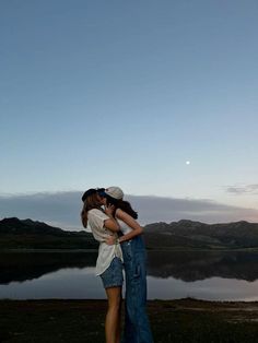 two people standing next to each other in front of a lake