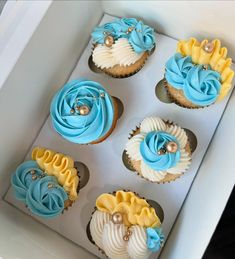 six cupcakes in a box with blue and yellow frosting on them,