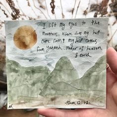 a hand holding up a piece of paper with a poem written on it and mountains in the background