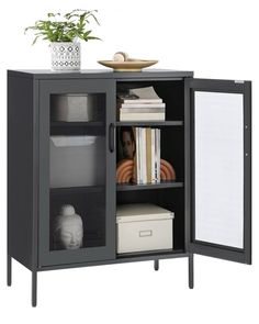 an open cabinet with some books and a vase on it's top shelf next to a plant