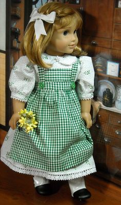 a doll with blonde hair wearing a green and white checkered dress holding a yellow flower