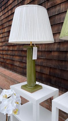 two white chairs and a green table with a lamp on it in front of a house