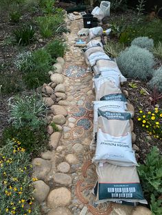 several bags of cement sitting on the side of a stone path next to flowers and plants