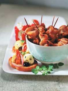 a bowl filled with skewers of food on top of a white plate next to other foods