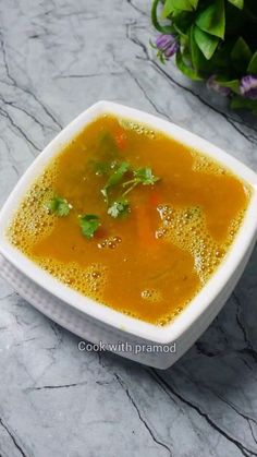 a white bowl filled with soup sitting on top of a table next to a potted plant